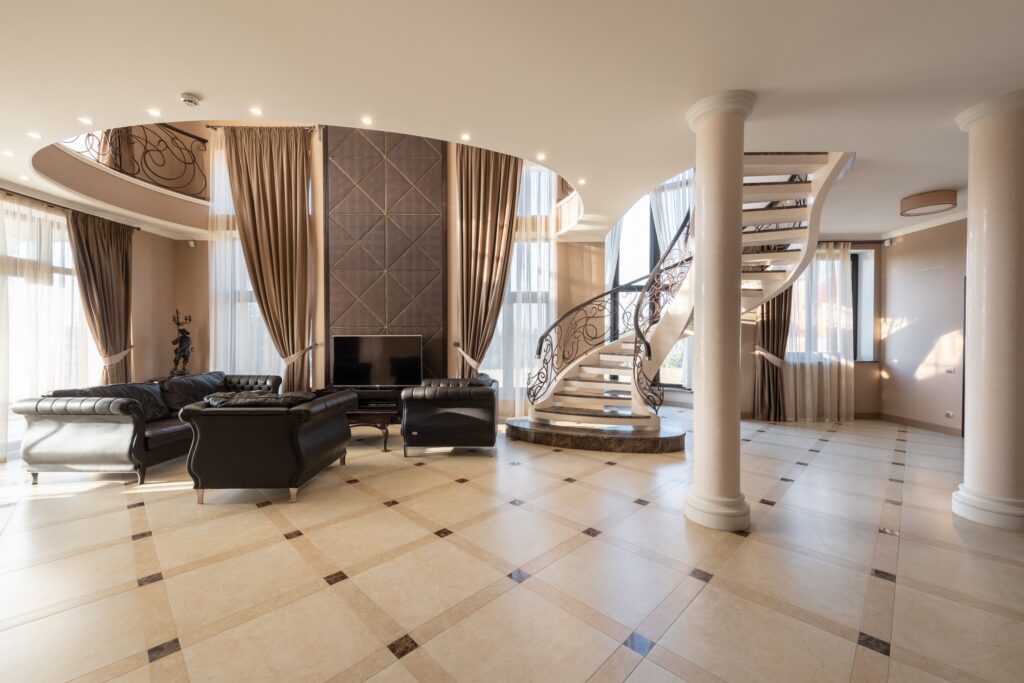 Interior of spacious hallway of classic styled villa with columns and comfortable leather sofa and armchair placed near spiral staircase